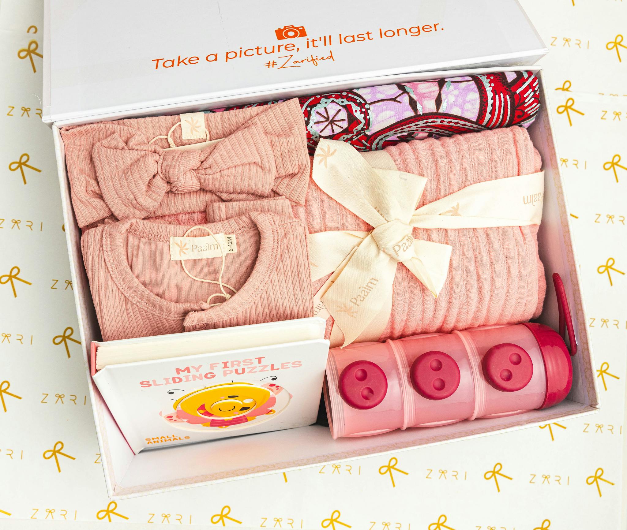 Adorable baby gift box featuring pink clothing, a puzzle book, and storage containers.